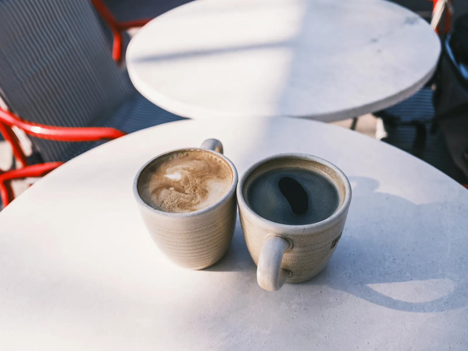 Two ceramic cups of coffee on a round white café table.